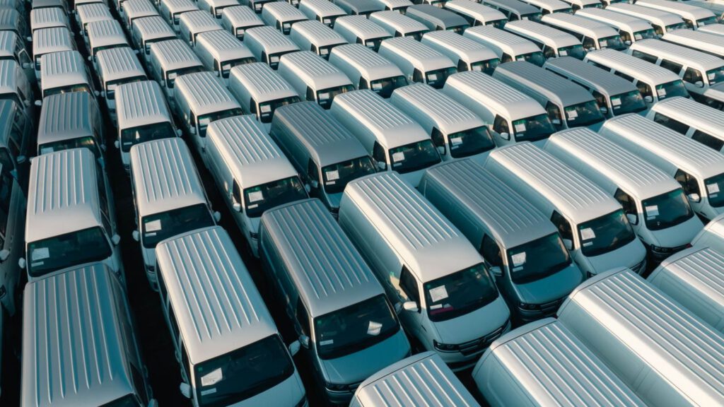 Luftaufnahme vieler gleichartiger weißer Transporter, dicht in Reihen abgestellt