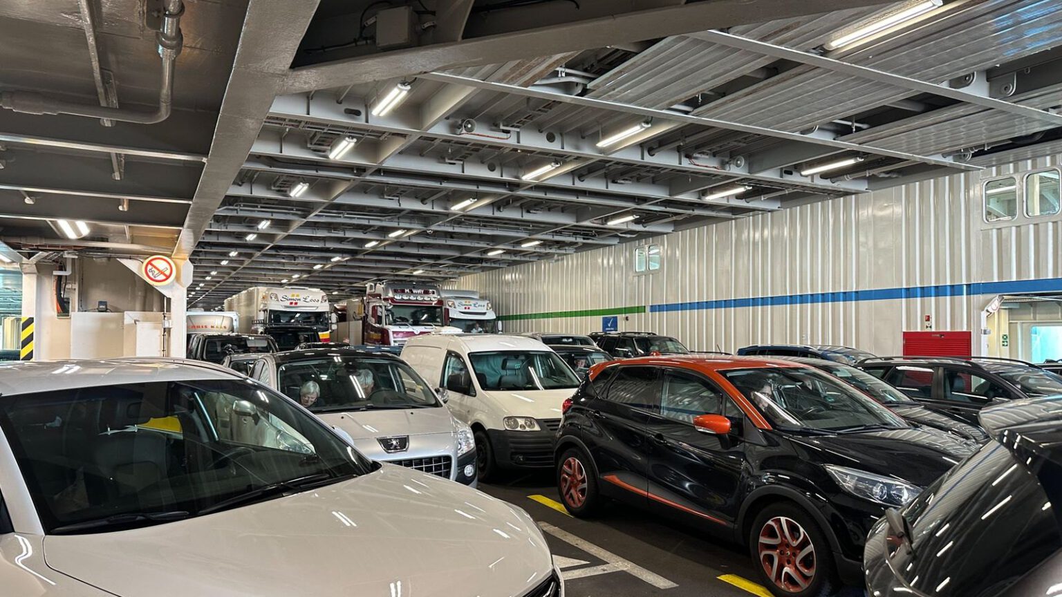 Geschlossenes Fahrzeugdeck einer Fähre mit dicht geparkten Pkw, Transportern und Lkw