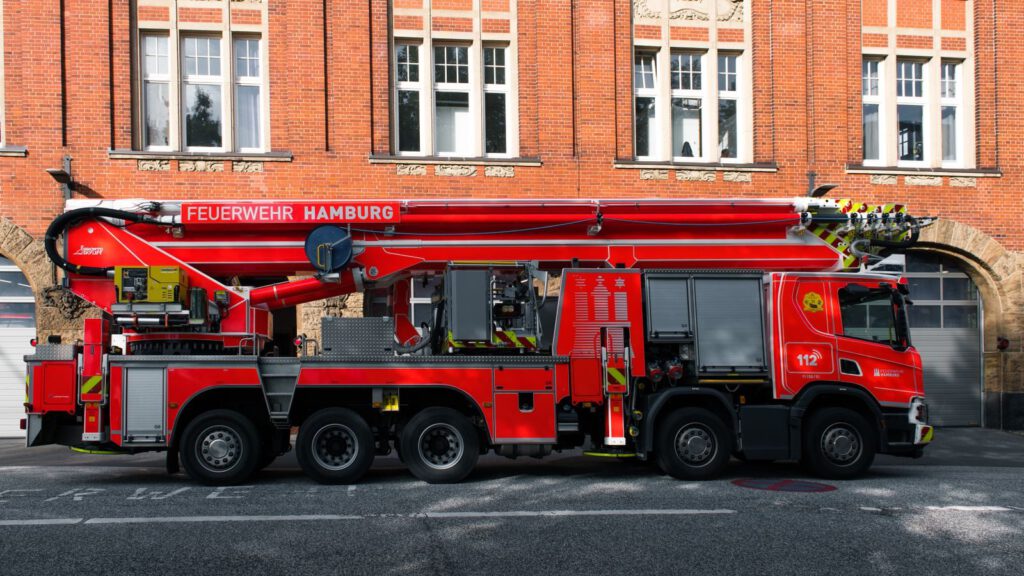 Rotes Drehleiterfahrzeug der Feuerwehr vor einem Backsteingebäude in Hamburg