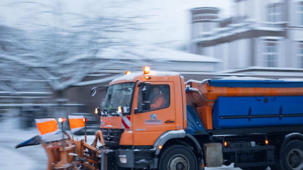 Orangefarbenes Räumfahrzeug im Winterdienst auf einer verschneiten Straße